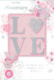 The photo shows a romantic anniversary card whose design echoes the softness of an English spring garden, reminiscent of the calm streets and leafy corners around Thames Ditton village. At the centre of the front cover, the word LOVE is spelled out in large, raised letters, each one filled with soft pastel pink and dusted with fine glitter that gives a gentle, silvery sheen. The letterforms are smooth yet subtly textured, inviting gentle touch in the same way one might instinctively brush the petals of a favourite flower in a bouquet. Instead of a plain surround, the card's blush-pink background acts like a canvas for delicate illustrations of flowers and swirling vines. These blooms unfurl in tones of blush, mauve, pearlescent white, and cool grey, with touches of silver highlighting certain petals and leaves, similar to how a florist might add a hint of metallic ribbon to elevate an anniversary arrangement. The lines are fine and flowing, with small petals, curls, and occasional tiny butterflies giving the impression of movement without overwhelming the eye. The composition feels light and balanced, creating a sense of treasured intimacy, much like sharing a quiet anniversary dinner at home after a stroll along Weston Green. At the top or centre, the words On Our Anniversary appear in a refined script, while nearer the bottom, the tender phrase I love you today and always is written in matching, understated lettering. Together, the colours, textures, and gentle sparkle create an image of a card that is soft-spoken yet profoundly heartfelt, ideal for commemorating a shared journey of love in Thames Ditton.